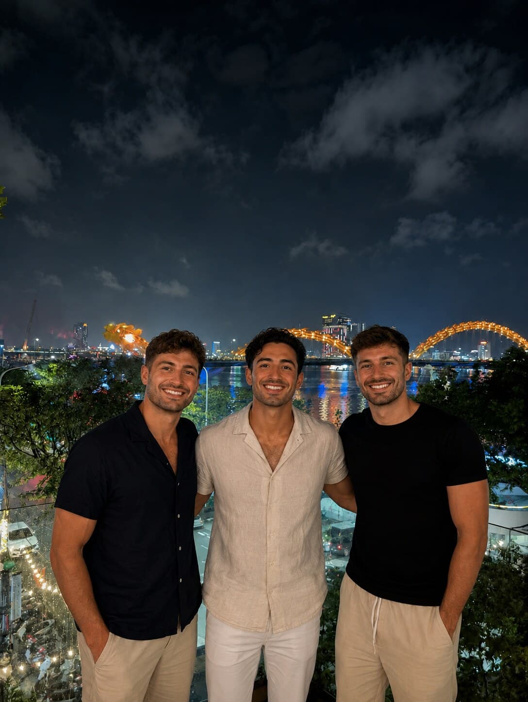 The three Nxeon co-founders on a rooftop in Da Nang, Vietnam, with the Dragon Bridge lit up behind them at night
